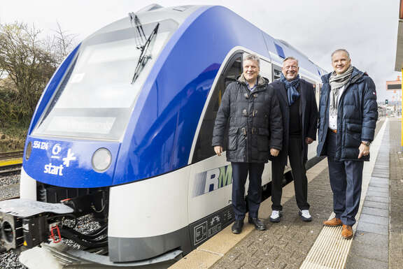 3 Männer stehen neben einer blau-weiß lackierten Bahn