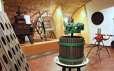 Vergrößerte Ansicht: Ausstellungsraum mit Weinpresse, einem Handwagen und weiteren Geräten