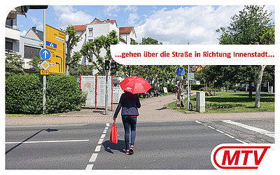Eine Frau mit rotem MTV-Regenschirm überquert eine Straße: ...gehen über die Straße in Richtung Innenstadt...
