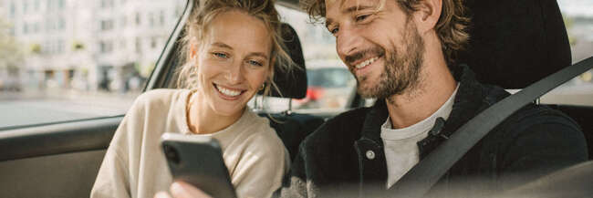 Mann und Frau sitzen in einem Auto und schauen auf ein Smartphone.