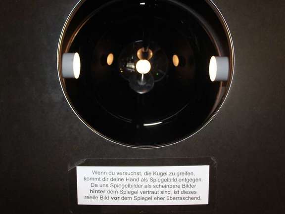 Vergrößerte Ansicht: schwarze Wand mit rundem Loch, darinnen Lichter und Spiegel