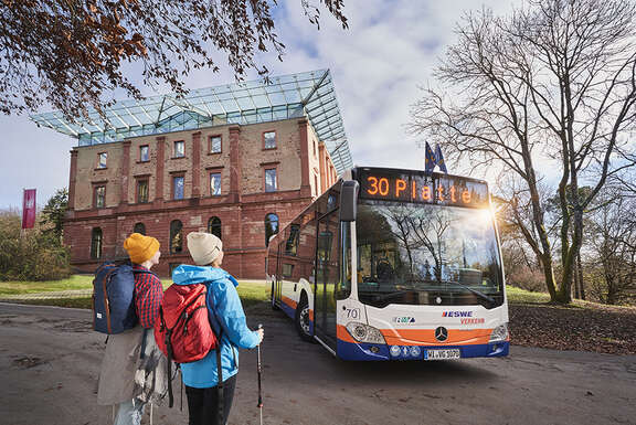 Ein Bus der Linie 30 steht vor dem Jagdschloss Platte. Zwei Wanderer gehen auf ihn zu.