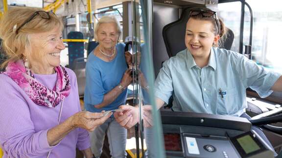 Seniorin kauft eine Fahrkarte im Bus.