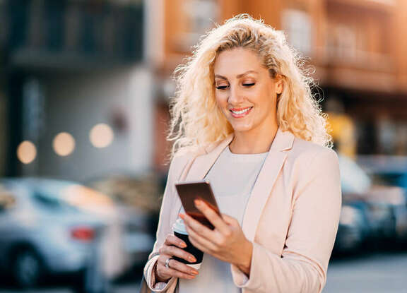 Smiling blond woman on the street looking on her mobile phone