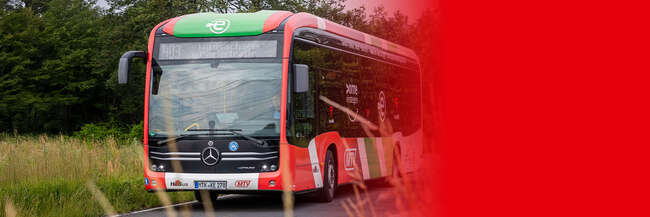 Roter Elektrobus im MTV-Design fährt auf einer Landstraße durch eine grüne Landschaft.