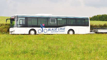 Vergrößerte Ansicht: Ein weißer Bus der Blauen Linie mit Fahrradanhänger fährt durch eine sommerliche Landschaft