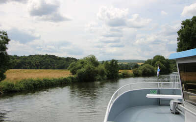 Blick vom Schiff im Vordergrund auf offene Landschaft mit Feldner, Hügeln und Bäumen