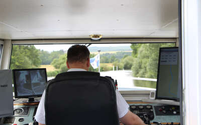 Blick durch Führerstand über den Rücken des Kapitäns auf den Fluss