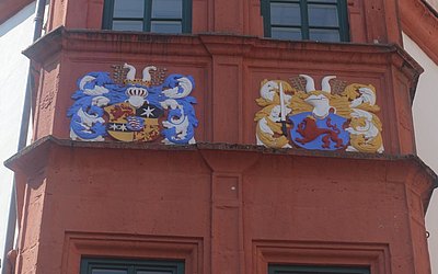 Vergrößerte Ansicht: Zwei bunte Wappen an roter Hausfassade