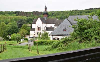 Historisches Gebäude mit Kirchturm umgeben von Wald und Weinberg