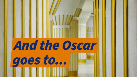 Mehrere weiße Säulen einer U-Bahnstation mit goldenen Streifen als Verziehrung. In einem orangefarbenen Textbalken steht: "And the Oscar goes to...".