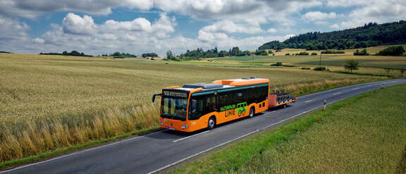 Ein orangefarbener Bus mit Fahrradanhänger fährt übers Land