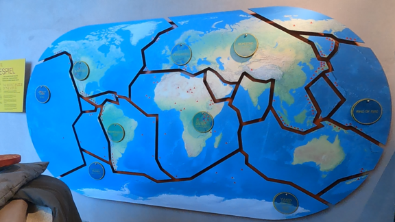 Weltkarte an der Wand. Hinter runden Plaketten werden verschiedene Orte erklärt
