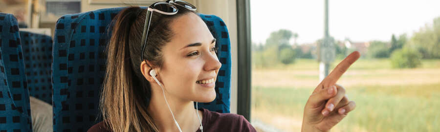 Junge Frau in der Bahn mit Handy und Kopfhörern deutet auf Fenster