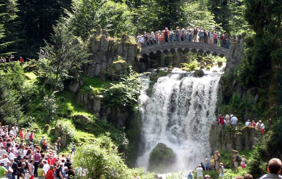 Personen stehen auf einer Brücke an einem Wasserfall.