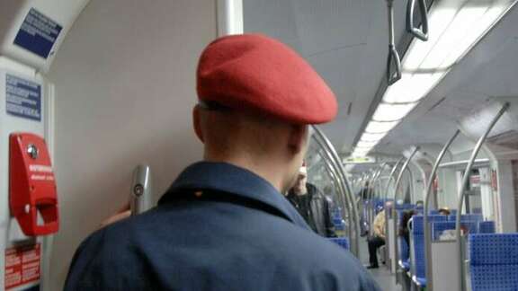 Man with red cap and blue uniform seen from behind in a suburban train