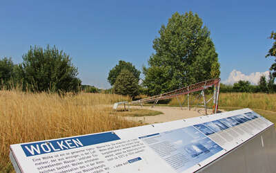 Vergrößerte Ansicht: Informationstafel mit Blick über eine Wiese mit Bäumen zum blauen Himmel