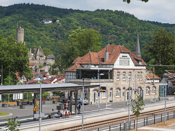Vergrößerte Ansicht: altes Bahnhofsgebäude mit modernem Glas-Anbau, davor Bahnsteig mit Gleis, dahinter Wald