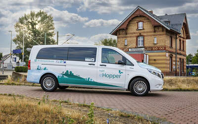 Ein Kleinbus steht vor dem Bahnhofsgebäude Obertshausen, Aufschrift: On-Demand-Shuttle eHopper