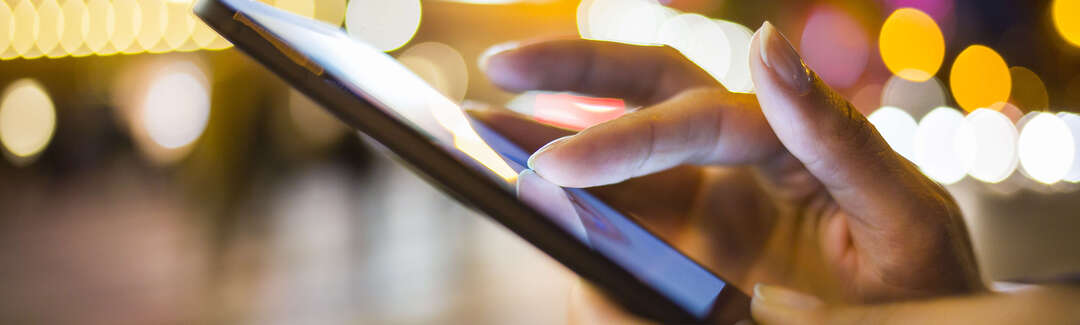 Hände die ein Smartphone bedienen draußen bei Nacht