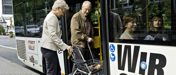 Senioren mit Rollator steigen in einen Bus.