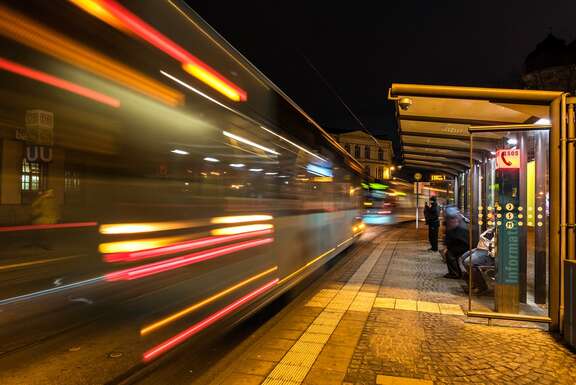 Kunstfoto: Straßenbahn als Lichtstreifen fährt an Haltestelle vorbei. 