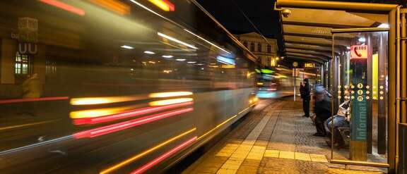 Kunstfoto: Straßenbahn als Lichtstreifen fährt an Haltestelle vorbei. 