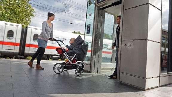 Frau mit Kinderwagen auf Bahnsteig steigt in einen Aufzug