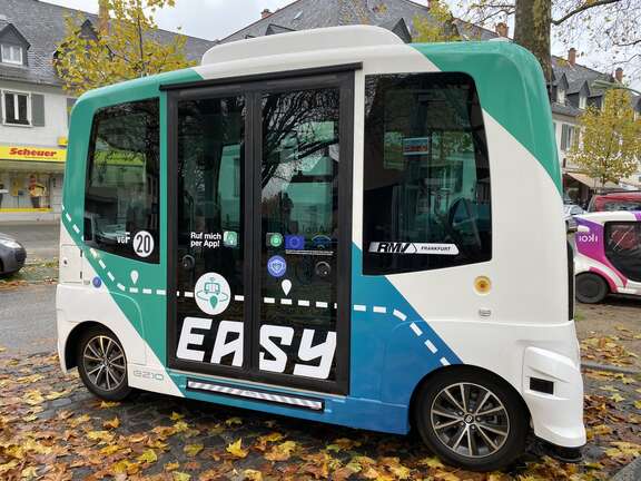 Ein Shuttlebus mit der Aufschrift "Easy" und einer grün-blau-weißen Lackierung steht auf der Straße.