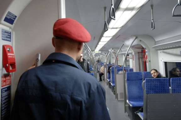 Man with red cap and blue uniform seen from behind in a suburban train