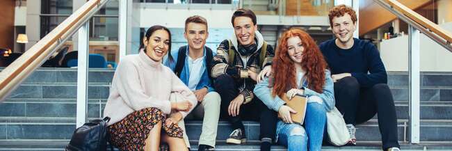 Fünf Schülerinnen und Schüler sitzen in einem Gebäude auf Treppenstufen 