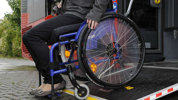 Nahaufnahme Frau in Rollstuhl fährt Rampe hinab. Link zu FAQ Barrierefreies Reisen