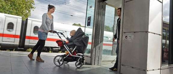 Frau mit Kinderwagen auf Bahnsteig steigt in einen Aufzug