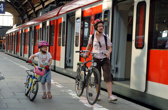 Frau und Mädchen schieben ihre Fahrräder am Bahnsteig neben Zug mit geöffneten Türen