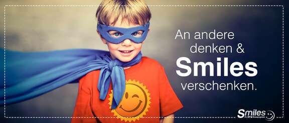 Junge mit Umhang, Augenmaske und Smiles-T-Shirt. Schrift: An andere denken & Smiles verschenken.