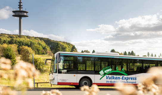Bus des Vulkan-Express vor der Silhouette des Fernsehturmes auf dem Hoherodskopf