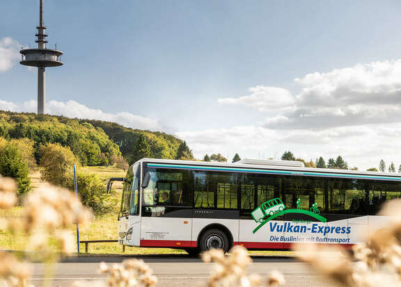 Bus des Vulkan-Express vor der Silhouette des Fernsehturmes auf dem Hoherodskopf
