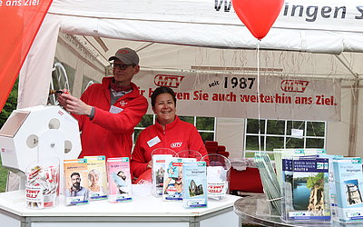 Zwei MTV-Mitarbeiter stehen im Pavillon. RMV- und MTV-Flyer stehen zur Vergabe bereit.