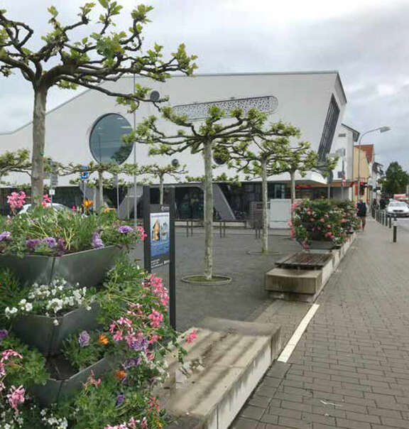 Weiterstädter Innenstadt Platz mit Sitzgelegenheiten, Blumen und Bäumen, ein Gebäude im Hintergrund.