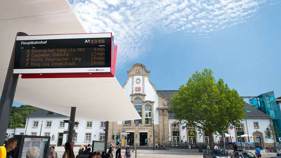 digitale Anzeigetafel am Bahnhofs-Vorplatz, im Hintergrund das Bahnhofs-Gebäude