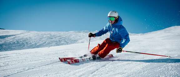 Ein bunt gekleideter Skifahrer fährt eine Piste hinunter