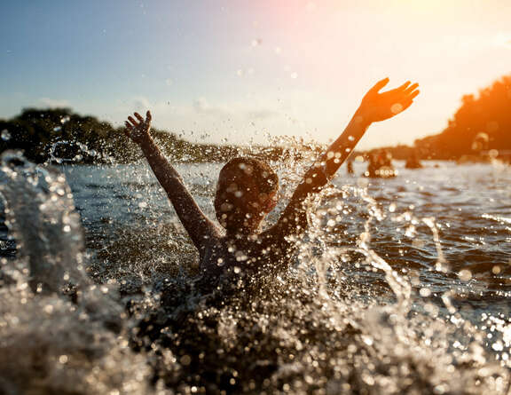 Ein Kind spielt bei Sonnenuntergang im See, Wasser spritzt herum