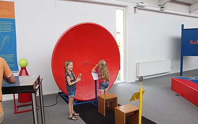 Vergrößerte Ansicht: Roter Parabolspiegel, davor zwei Mädchen
