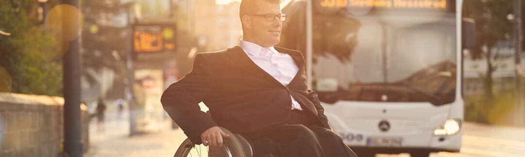 Rollstuhlfahrer blickt auf einen herannahenden Bus
