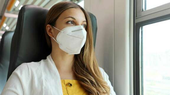 Junge Frau sitzt mit FFP2-Maske im Zug