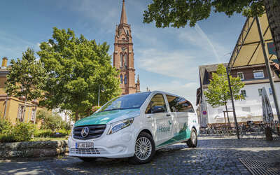 Ein weiß-grüner Kleinbus steht vor einer Kirche im Grünen. Aufschrift: eHopper