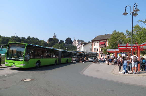 Drei Busse halten links, rechts warten Fahrgäste an der Haltestelle