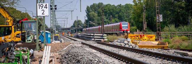 Neues Bahngleis, links Baustellenfahrzeuge, rechts S-Bahn auf bestehendem Gleis