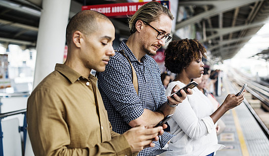 Personen mit Smartphone am Bahnhof