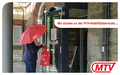 Eine Frau mit rotem MTV-Regenschirm verlässt das Gebäude: Wir starten an der MTV-Mobilitätszentrale... 